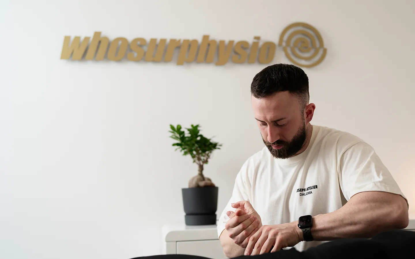 Physiotherapeut von Whosurphysio bei der Behandlung, im Hintergrund das Praxislogo